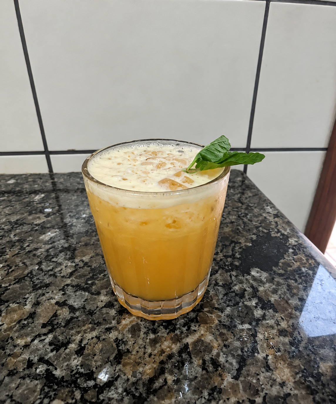 Drink amarelo em copo com espuma clara e hortelã.