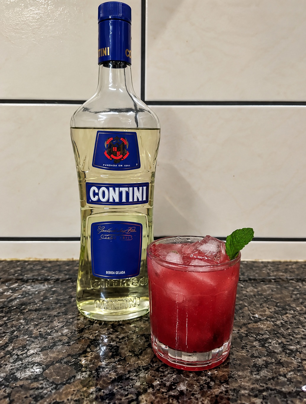 Drink vermelho com hortelã em copo, ao lado de uma garrafa Contini.