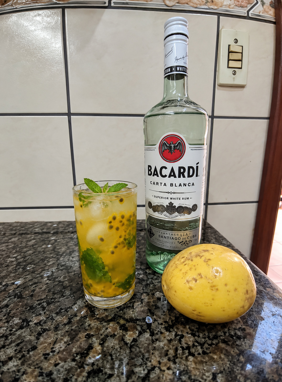 Mojito de maracujá com hortelã e sementes, ao lado de uma garrafa de rum branco.