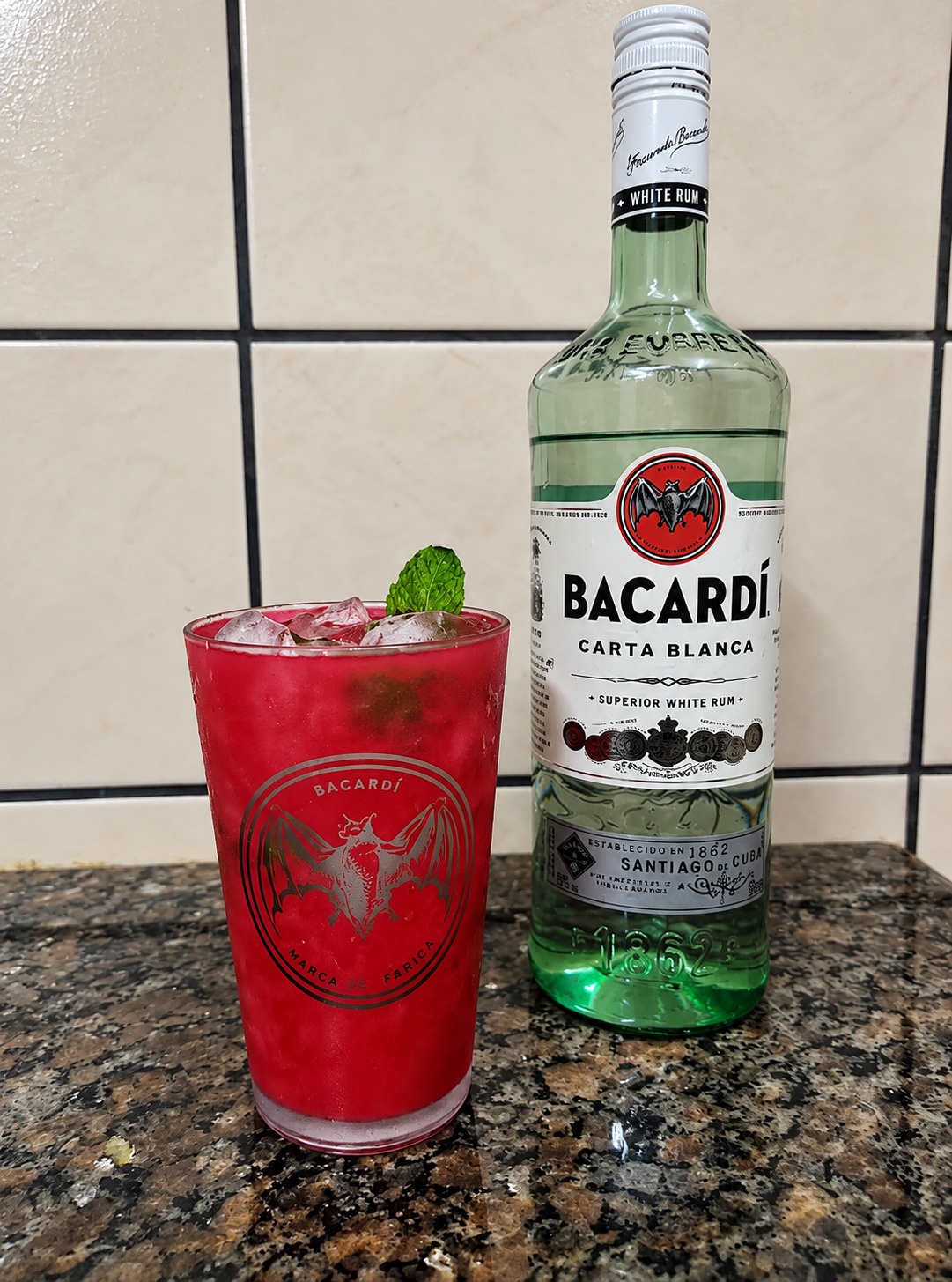 Mojito vermelho com hortelã em copo, ao lado de uma garrafa Bacardi.